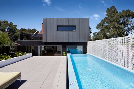 The modern home has a sleek, angular exterior with a large window and an inviting swimming pool.