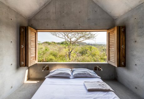 Minimalist concrete cabin with wooden shutters overlooking a lush green landscape.