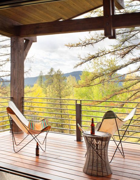 Cozy wooden cabin porch overlooking lush autumn foliage, with comfortable chairs and side table.