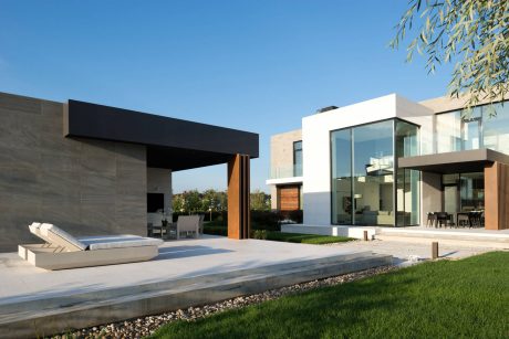 Sleek modern home with glass walls, stone patio, and lush landscaping.