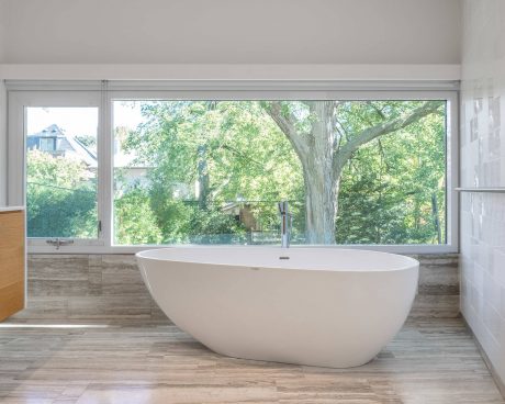 Spacious bathroom with freestanding tub and large windows overlooking lush greenery.