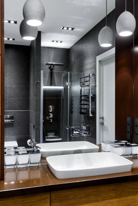 A modern, minimalist bathroom with sleek gray tiles, pendant lighting, and a floating vanity.