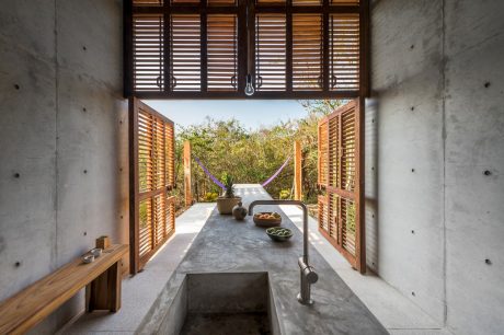 Rustic concrete kitchen with wooden shutters and a view to a lush outdoor space.