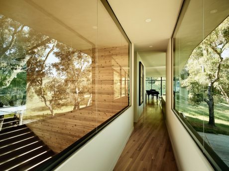 A modern, glass-enclosed hallway with wood paneling and a view of the surrounding trees.