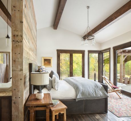 Rustic bedroom with exposed wood beams, pendant lighting, and large windows overlooking nature.