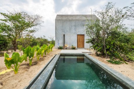 Minimalist concrete beach house with rectangular pool surrounded by lush greenery.
