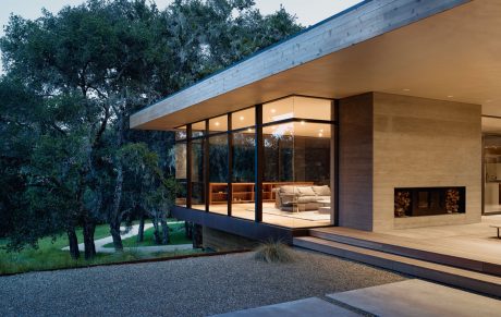 Modern single-story home with large glass walls, overhanging roof, and natural surroundings.