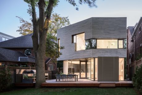 Contemporary two-story home with expansive windows, wooden deck, and landscaped backyard.