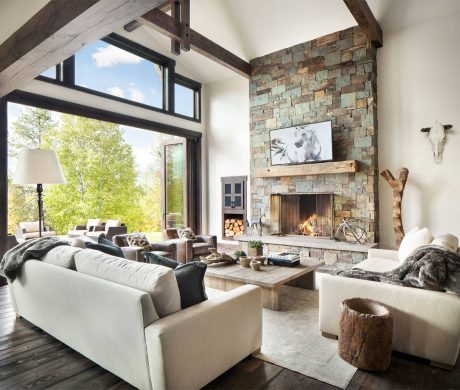 Spacious living room with high ceilings, stone fireplace, wood beams, and large windows.