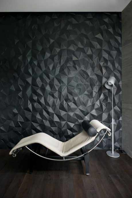 A modern chaise lounge chair in a room with an angular, textured black wall.