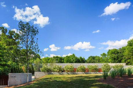 A modern concrete building surrounded by lush greenery, with a grassy lawn and garden beds.