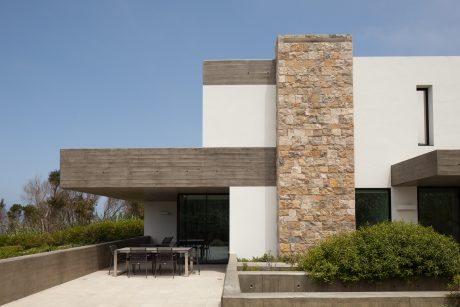 Modern concrete and stone exterior with covered patio, surrounded by greenery.