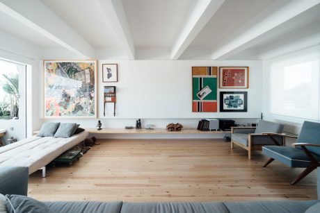 A spacious, minimalist living room with high ceilings, wooden floors, and a mix of modern and eclectic decor.
