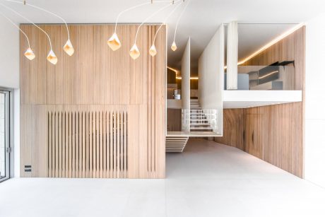 A modern, minimalist interior with wooden wall panels, pendant lighting, and a floating staircase.