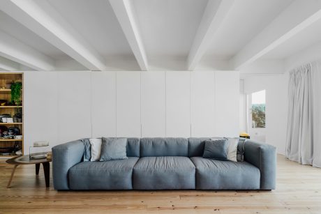 Large, plush gray sofa set against a white wall with high ceilings and wooden floors.