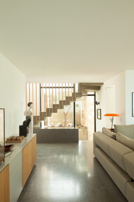 Minimalist living room with concrete floors, wooden staircase, and modern furnishings.