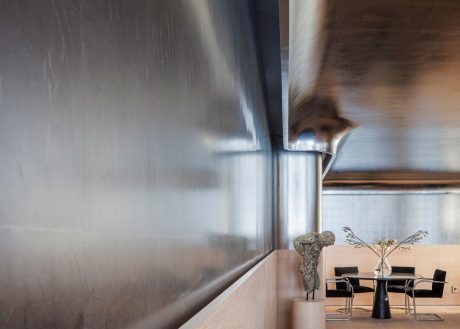 Modern, minimalist dining area with stainless steel wall, wooden table, and minimalist decor.