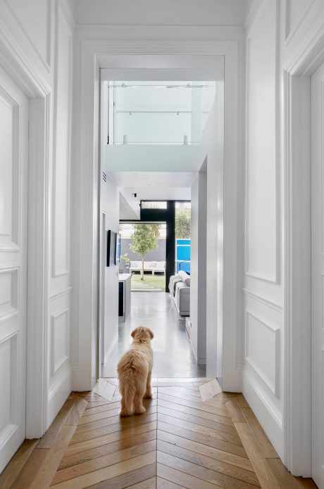 A bright, minimalist hallway with a sliding glass door leading to a modern living room.