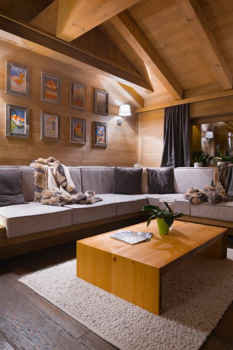 A cozy alpine-style living room with wooden beams, framed vintage posters, and a plush sectional.