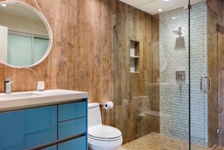 Rustic wood tiles, teal vanity, and mosaic shower tile create a modern yet warm bathroom.