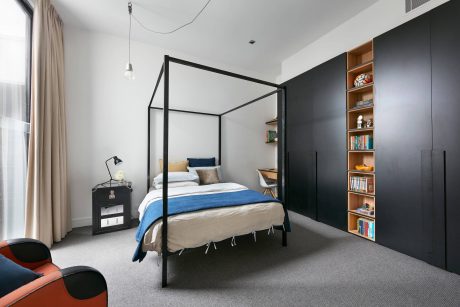 Minimalist bedroom design with black metal canopy bed, built-in shelving, and neutral tones.