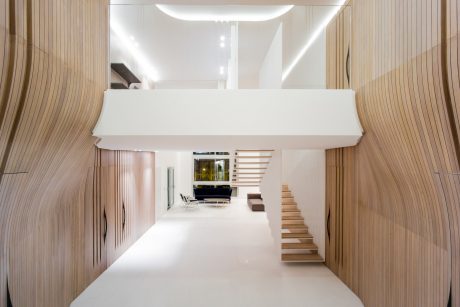 A modern, minimalist interior design with wood paneling, open staircase, and a mezzanine.