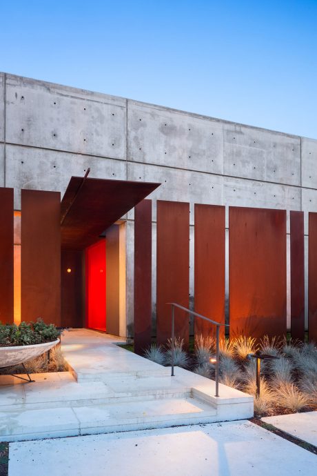 Striking concrete exterior with bold red accents and modern landscaping. Inviting entrance.
