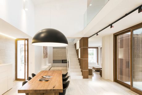 Modern minimalist living space with wooden accents, large pendant light, and open staircase.