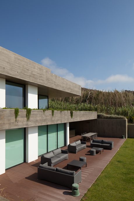 A modern concrete and glass structure with a spacious outdoor lounge area and lush greenery.