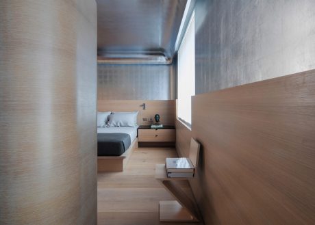 Minimalist bedroom with wooden walls, built-in nightstand, and wooden flooring.
