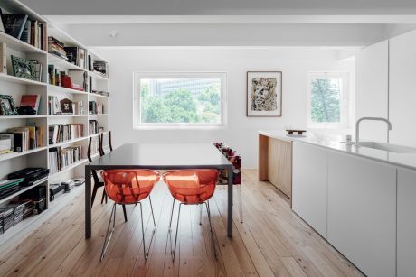 A bright, contemporary dining space with a bookshelf wall, red chairs, and wood floors.