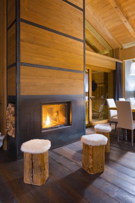 Rustic wooden cabin interior with a cozy fireplace, furry stools, and plush seating.