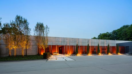 A modern, sleek building with warm, illuminated entryways, concrete walls, and landscaping.