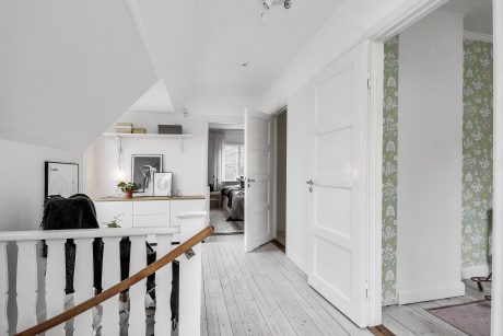 A bright, airy hallway with white walls, wooden floors, and a patterned curtain.