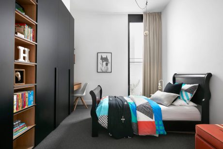 A modern, minimalist bedroom with sleek black furniture, colorful bedding, and built-in shelving.
