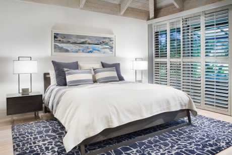 Cozy bedroom with wooden ceiling, shuttered windows, and stylish blue-patterned rug.