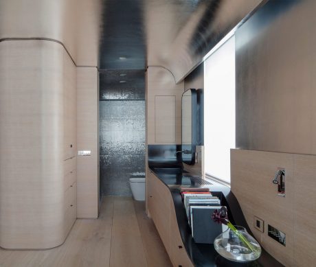 A modern, minimalist bathroom with sleek fixtures, warm wood tones, and an interesting textured wall.