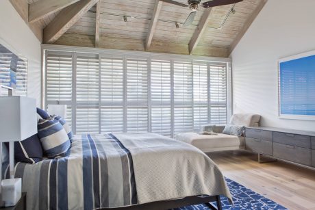 Cozy bedroom with wooden ceiling, shutter blinds, and coastal decor accents.