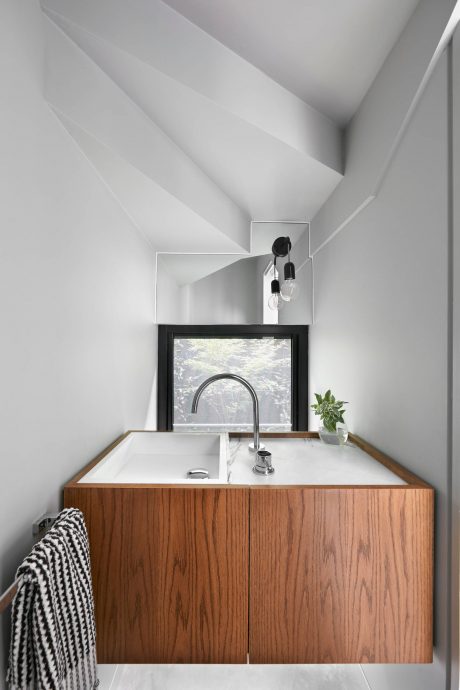 Modern bathroom with wood-paneled vanity, frameless window, and minimalist lighting.