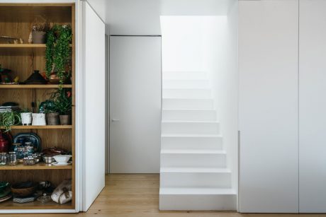 Minimalist white staircase leading to upper floor, with wooden shelves displaying various objects.