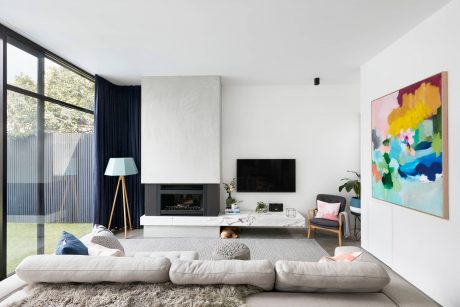 Modern open-plan living room with fireplace, artwork, and floor-to-ceiling windows.