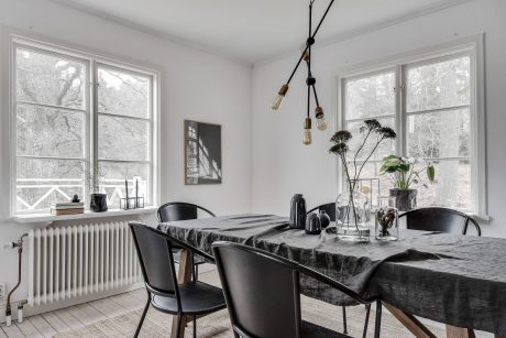 A cozy dining room with large windows, a black and wood table, and a hanging light fixture.