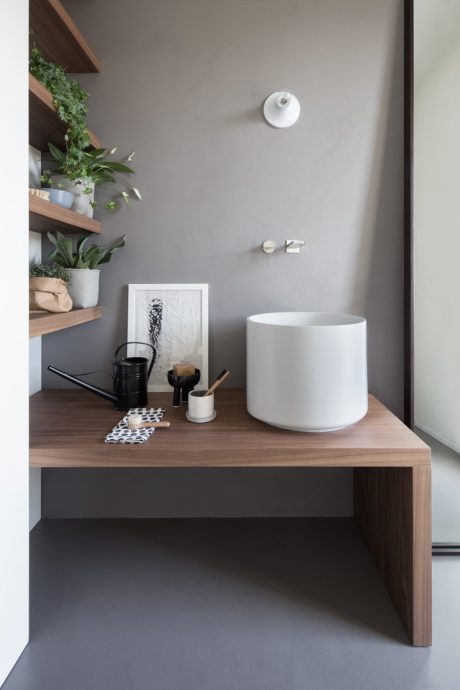 A modern bathroom vanity with a white circular sink, wooden shelving, and various accessories.