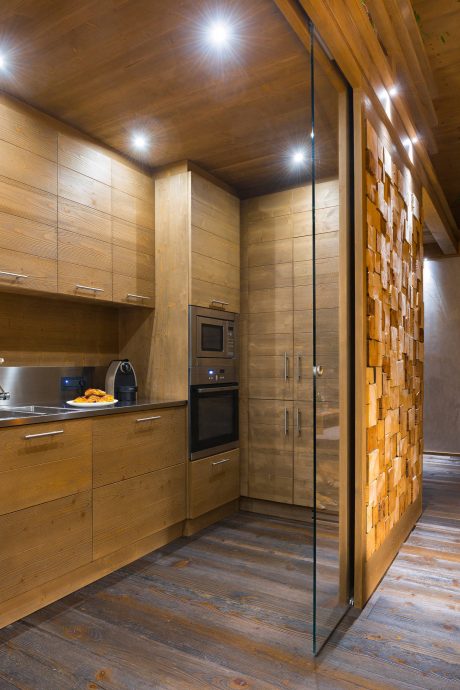 A cozy wooden kitchen with sleek cabinets, a brick accent wall, and recessed lighting.