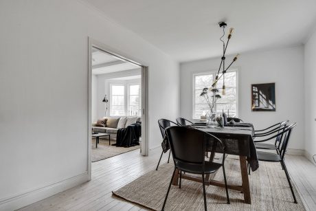 Minimalist dining room with large window, wooden floor, and modern light fixture.