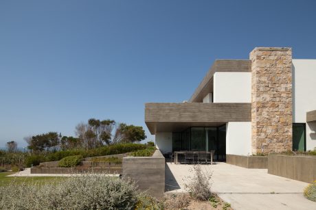 A modern, minimalist home with concrete, stone, and glass features against a blue sky.