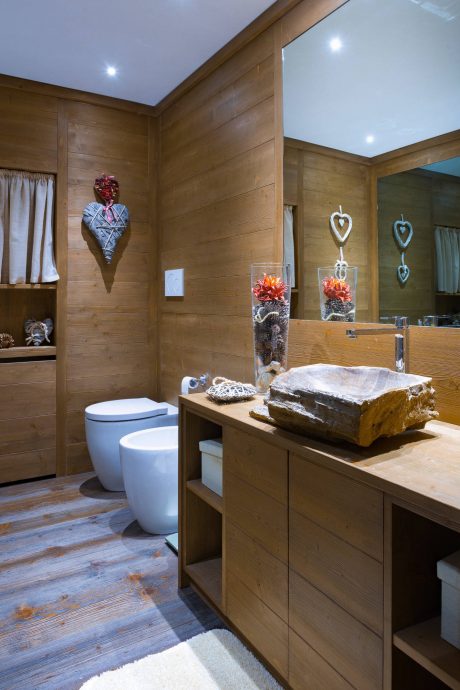 Cozy rustic bathroom with wooden paneling, stone vanity, and decorative hearts.
