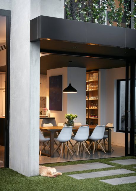 Sleek, modern kitchen-dining area with stylish black cabinetry, wooden table, and plush greenery.