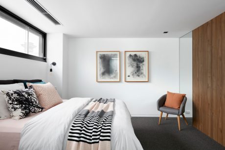 A minimalist bedroom with abstract artwork, a gray armchair, and wood paneling on the wall.