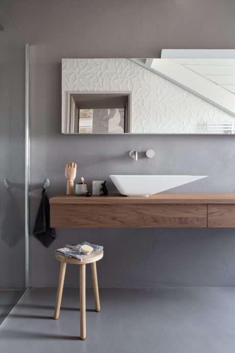 Minimalist bathroom design with textured white wall, wooden vanity, and modern vessel sink.